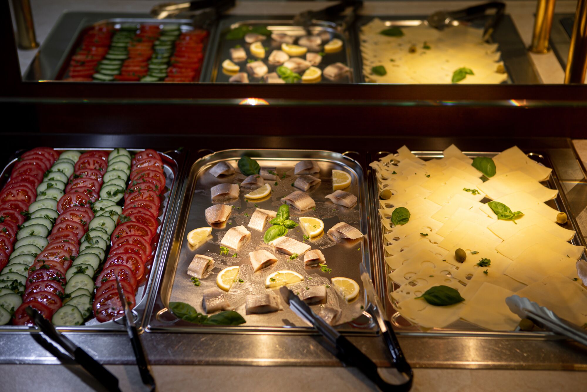 A buffet with various food items including sliced tomatoes, cucumbers, fish, and cheese.
