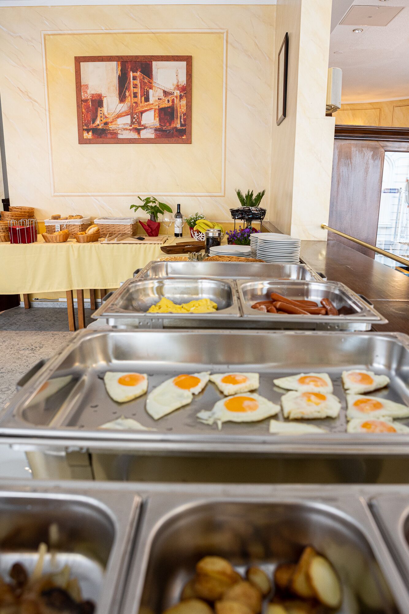 A buffet setup with various food items including eggs, sausages, and fruits.