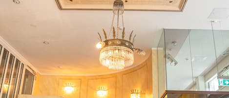 A grand staircase with a marble finish, a chandelier, and wall sconces.