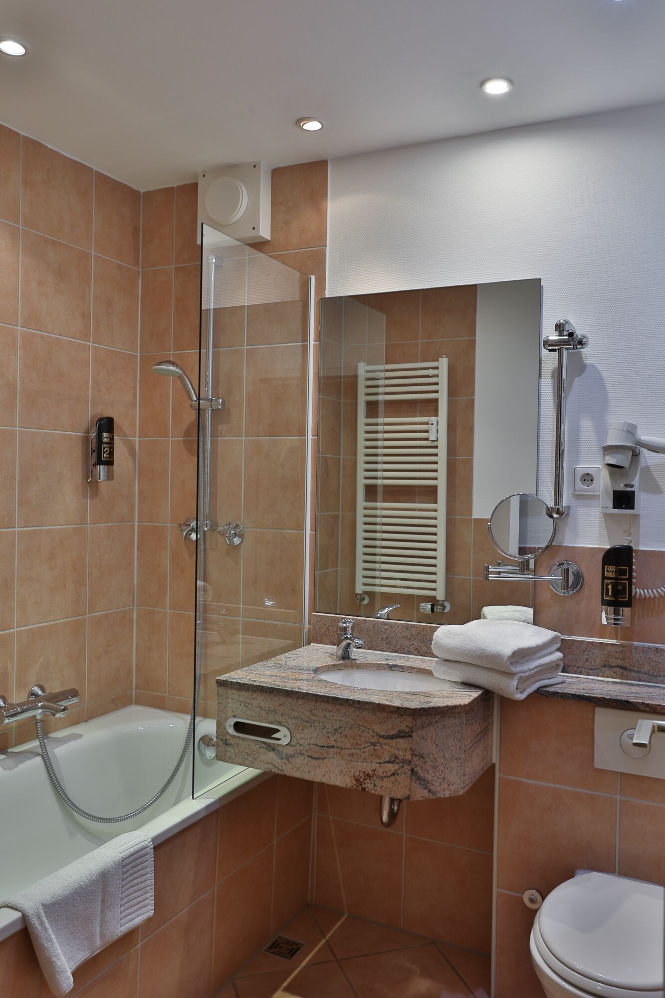 Un baño moderno con ducha de vidrio, bañera, tocador con lavamanos e inodoro.