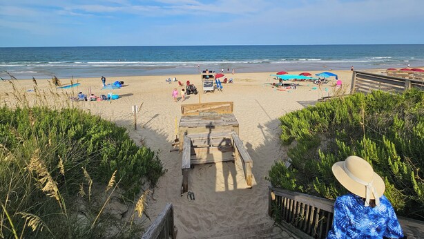 A beach with a wooden boardwalk leading to the shore, surrounded by greenery. - Condo located in Barrier Island Station Duck Resort Unit 505A (Duck)