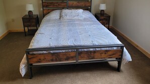 A neatly made bed with a wooden headboard, two bedside tables with lamps, and a carpeted floor. - Wooded, peaceful setting 15 minutes from  the Lake! (Sandpoint)
