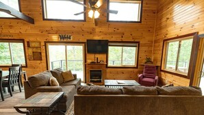 A cozy cabin interior with a large wooden ceiling, a fireplace, a TV, and a dining area. - Luxury mountain cabin (Zoe)
