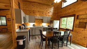 A cozy cabin interior with a wooden interior, a dining area with a table and chairs, a kitchen with cabinets and appliances, and a window providing a view of the outdoors. - Luxury mountain cabin (Zoe)