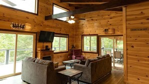 A log cabin interior with a wooden ceiling, large windows, a fireplace, a television, and a sofa. - Luxury mountain cabin (Zoe)
