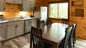 A wooden cabin interior with a dining table, chairs, a kitchen area, and a ceiling fan. - Luxury mountain cabin (Zoe)