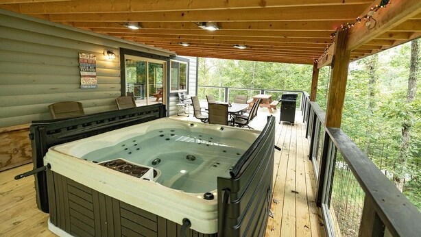 A hot tub on a wooden deck with outdoor seating and a view of trees. - Luxury mountain cabin (Zoe)