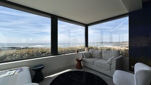 A modern living room with a large window overlooking a beach and cityscape. - Maison Avec Vue Panoramique sur L'océan (BATZ SUR MER)