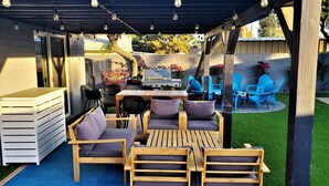Eine Terrasse im Freien mit Holzmöbeln, einem Grill und blauen Stühlen.