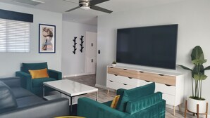Ein modernes Wohnzimmer mit Türkis-Sofas, einem weißen Couchtisch, einem Flachbildfernseher auf einer weißen Konsole und einem Deckenventilator.