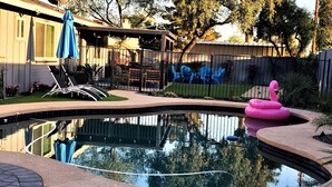 Ein Garten mit Swimmingpool, einem Flamingo-Schwimmpfau und einer überdachten Terrasse.