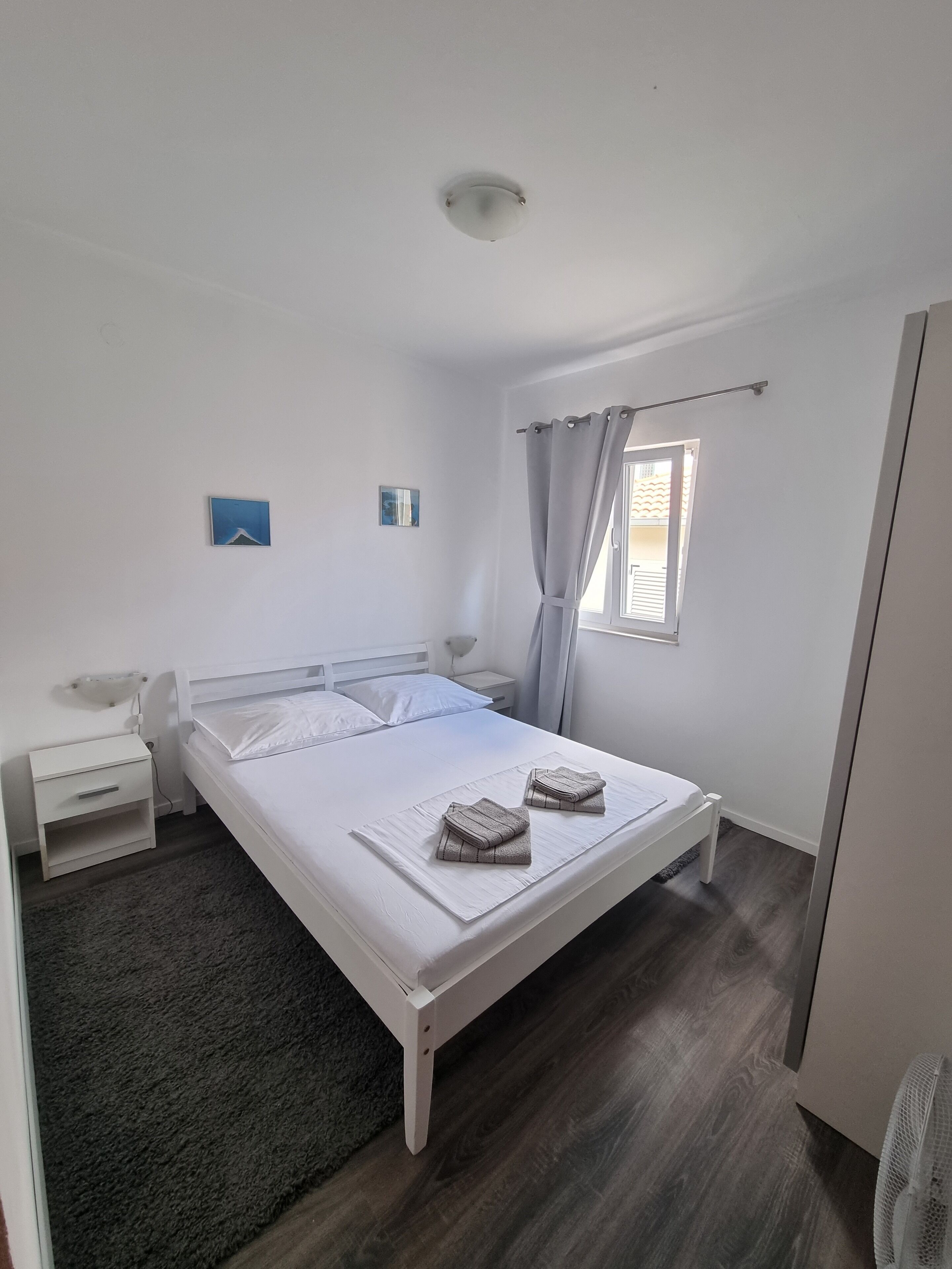 A bedroom with a bed, a bedside table, a nightstand, a window with curtains, and a ceiling light.