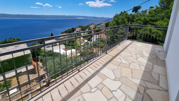 A balcony with a stone floor and metal railing overlooking a coastal area with houses and greenery. - Apartment Maya 1 (Marušici)