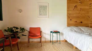 Una habitación con techo de madera, cama con ropa de cama blanca, una silla roja, una mesita y una planta verde.