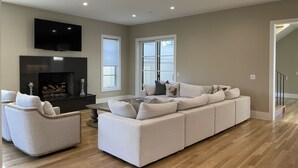 Un salon spacieux avec un grand canapé d’angle, une cheminée et un téléviseur à écran plat fixé au mur.