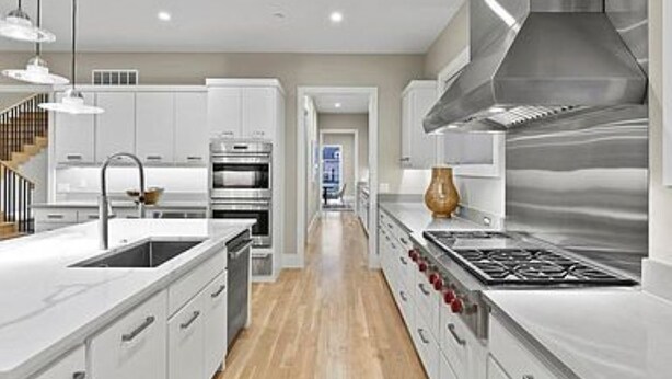 Une cuisine moderne avec des meubles blancs, des appareils en acier inoxydable et un plancher en bois.