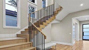 Un escalier avec des marches en bois et des rampes noires, menant à un palier dont le sol est de couleur claire.