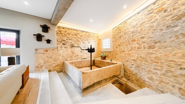 A modern bathroom with a stone wall, a freestanding bathtub, and a wooden bench.