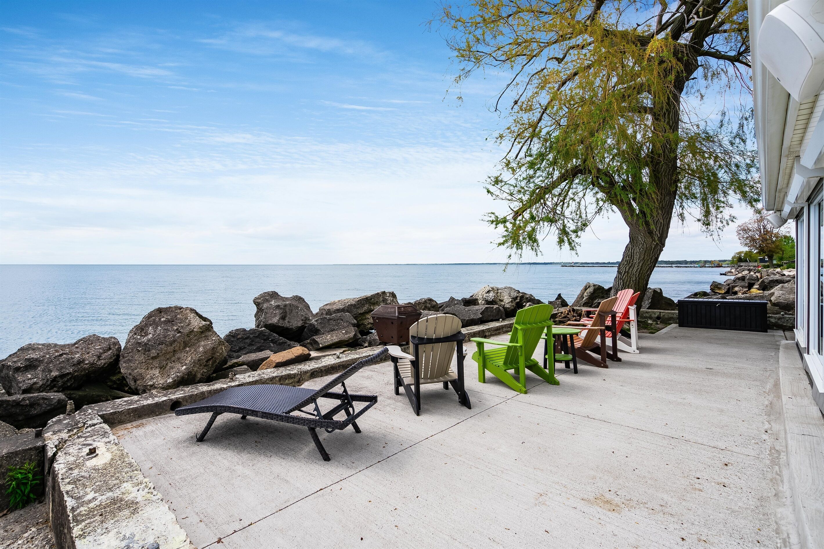 Een terras met buitenmeubilair, uitzicht op het water en een boom.