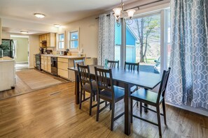 A spacious kitchen with a dining area, large windows, and a view of the outdoors. - River Road: 3 br, a/c, garage, and river views in lower Village! (Stowe)