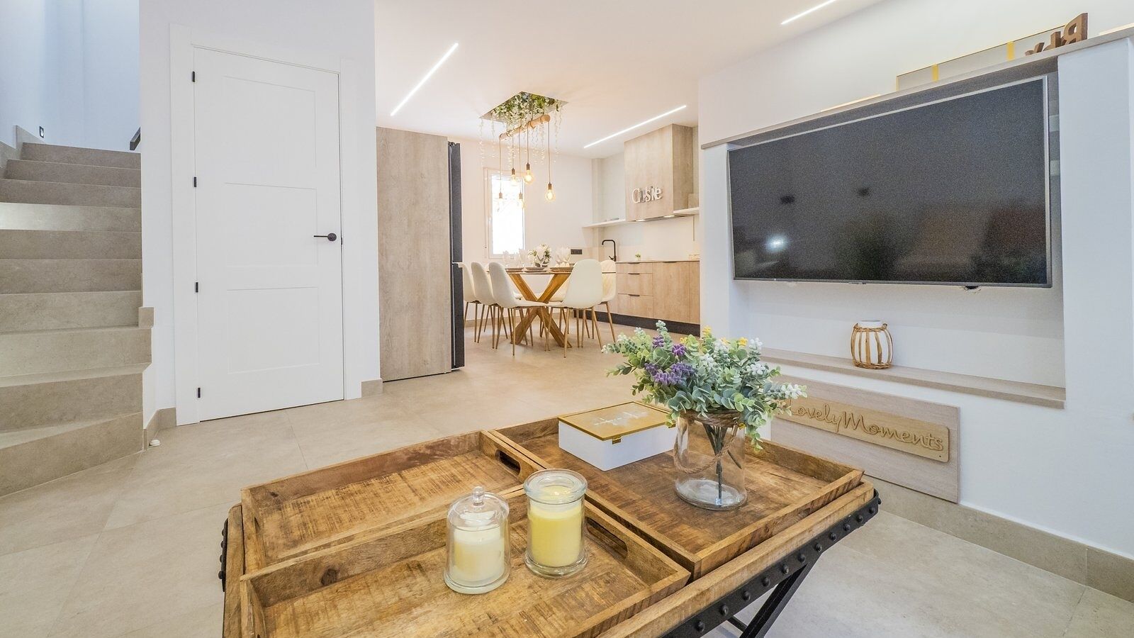Een moderne keuken met een eethoek, een tv aan de muur en een houten tafel met een vaas en kaarsen.