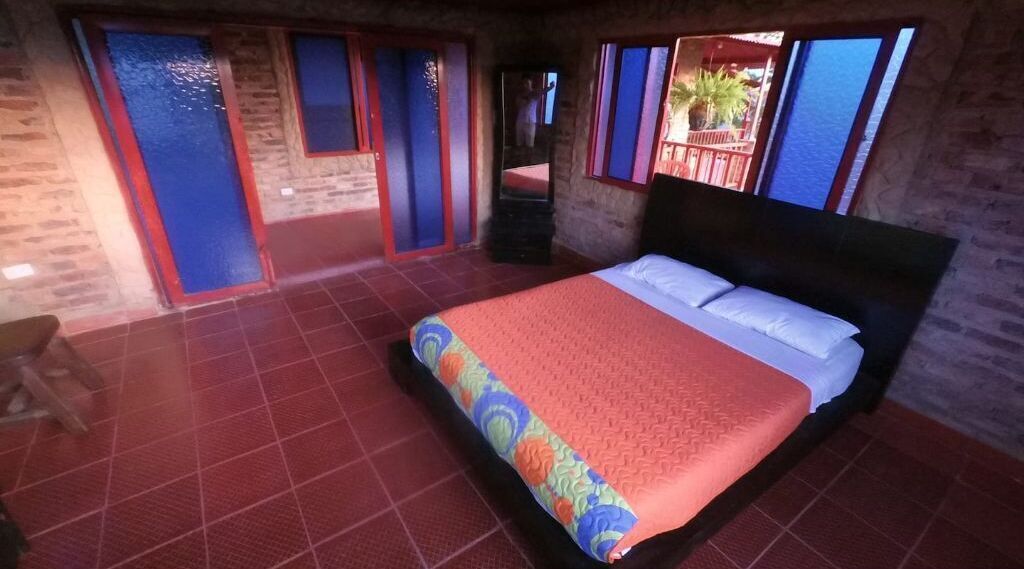 Un dormitorio con una cama grande, suelo de baldosas rojas y vistas al balcón exterior.