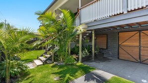 Ein modernes, zweistöckiges Haus mit überdachter Terrasse, Garage und gepflegtem Garten mit Palmen.