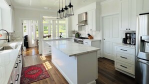 Une cuisine spacieuse avec des meubles blancs, un grand îlot central, un four encastré et un réfrigérateur en acier inoxydable.