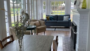 Un salon spacieux avec une cheminée, un coin repas comprenant une table et des chaises, et une grande fenêtre offrant une vue sur l’extérieur.