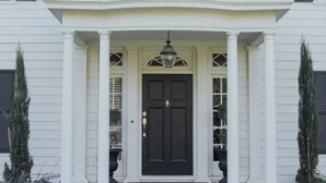 Un bâtiment blanc avec une porte d’entrée sombre, des colonnes et un balcon.