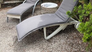 A patio area with two lounge chairs and a small round table, surrounded by greenery and a stone wall. - Dans Domaine Privé et Sécurisé Appt Type 2 Avec 3 Piscines , 2 Tennis (Cogolin)