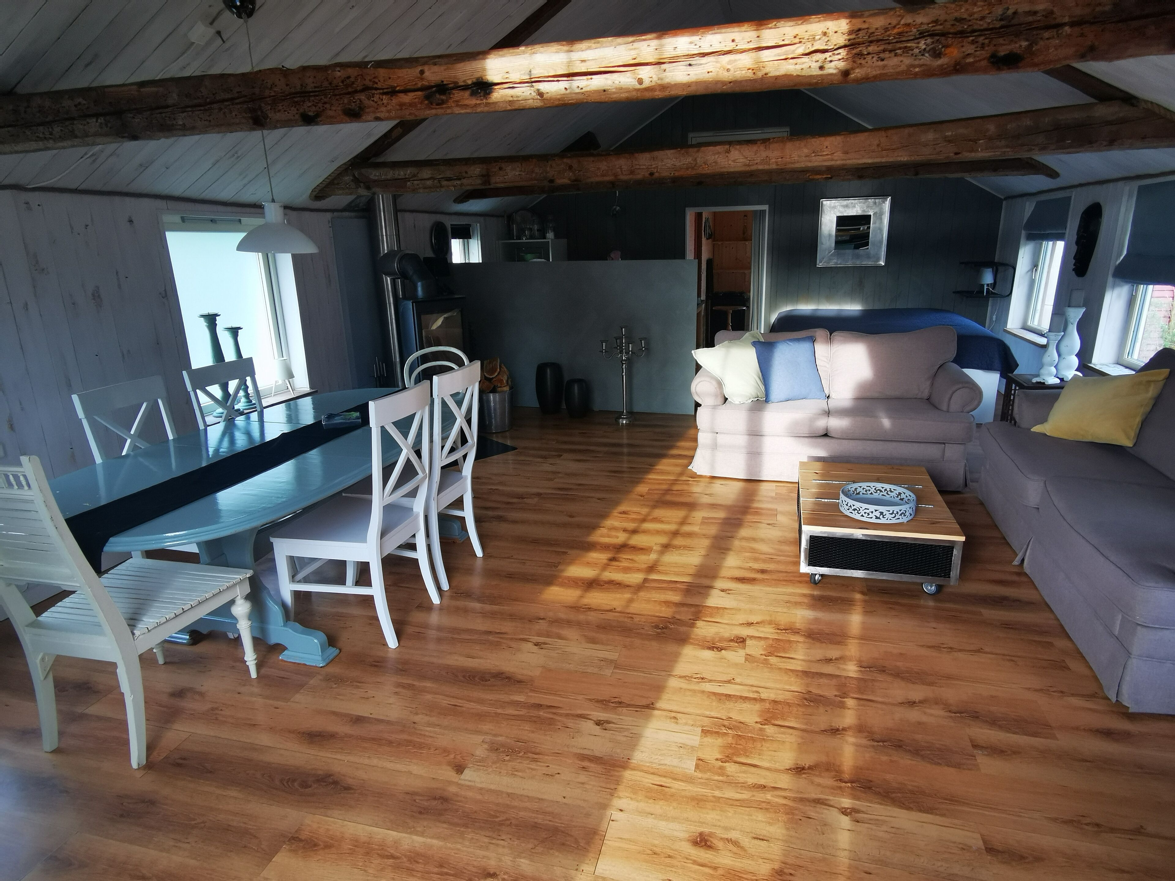 A spacious living area with a wooden floor, a dining table with chairs, a sofa, and a coffee table.
