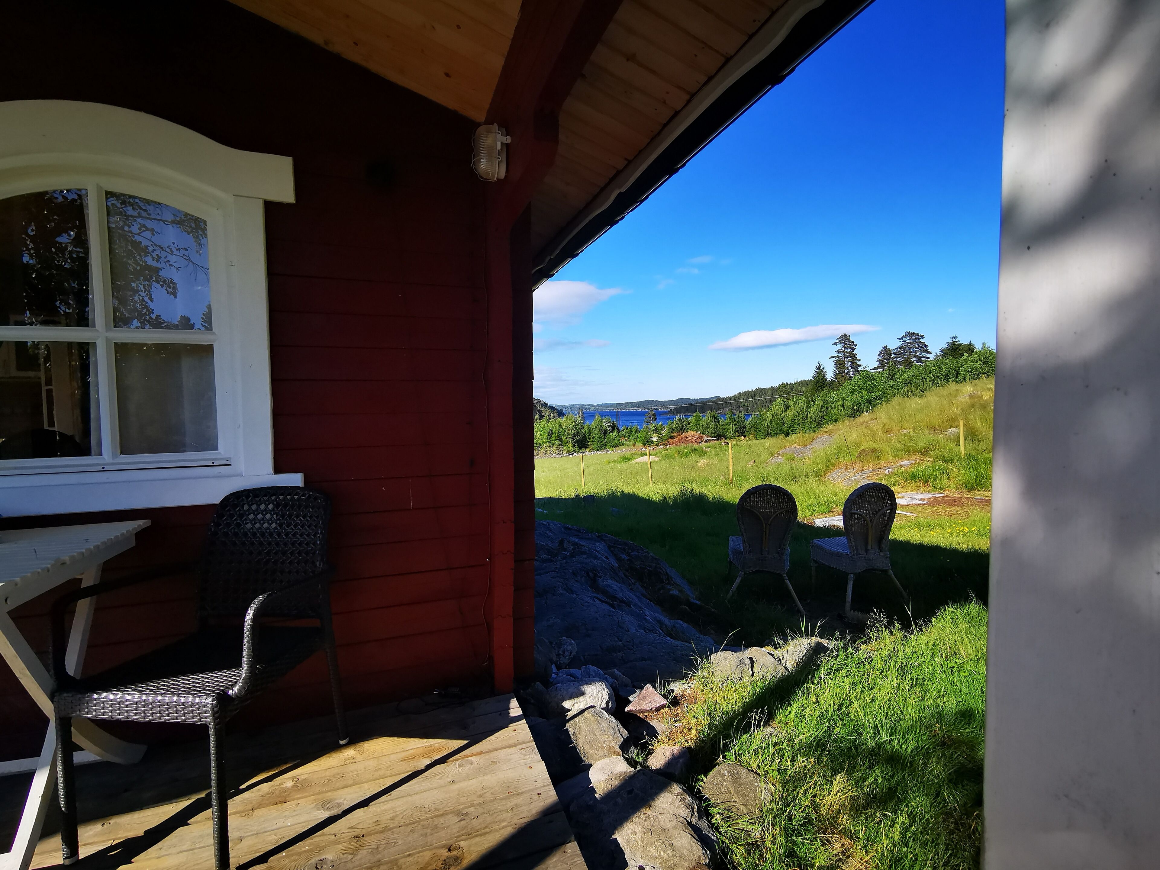 Eine Holterrasse mit zwei Korbstühlen, einem Tisch und Blick auf eine grüne Landschaft sowie ein Gewässer.