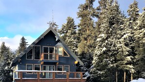 A two-story wooden cabin with a balcony, surrounded by snow-covered trees. - Spacious rental for 6 in lovely home with gorgeous views, minutes from resort (Girdwood)