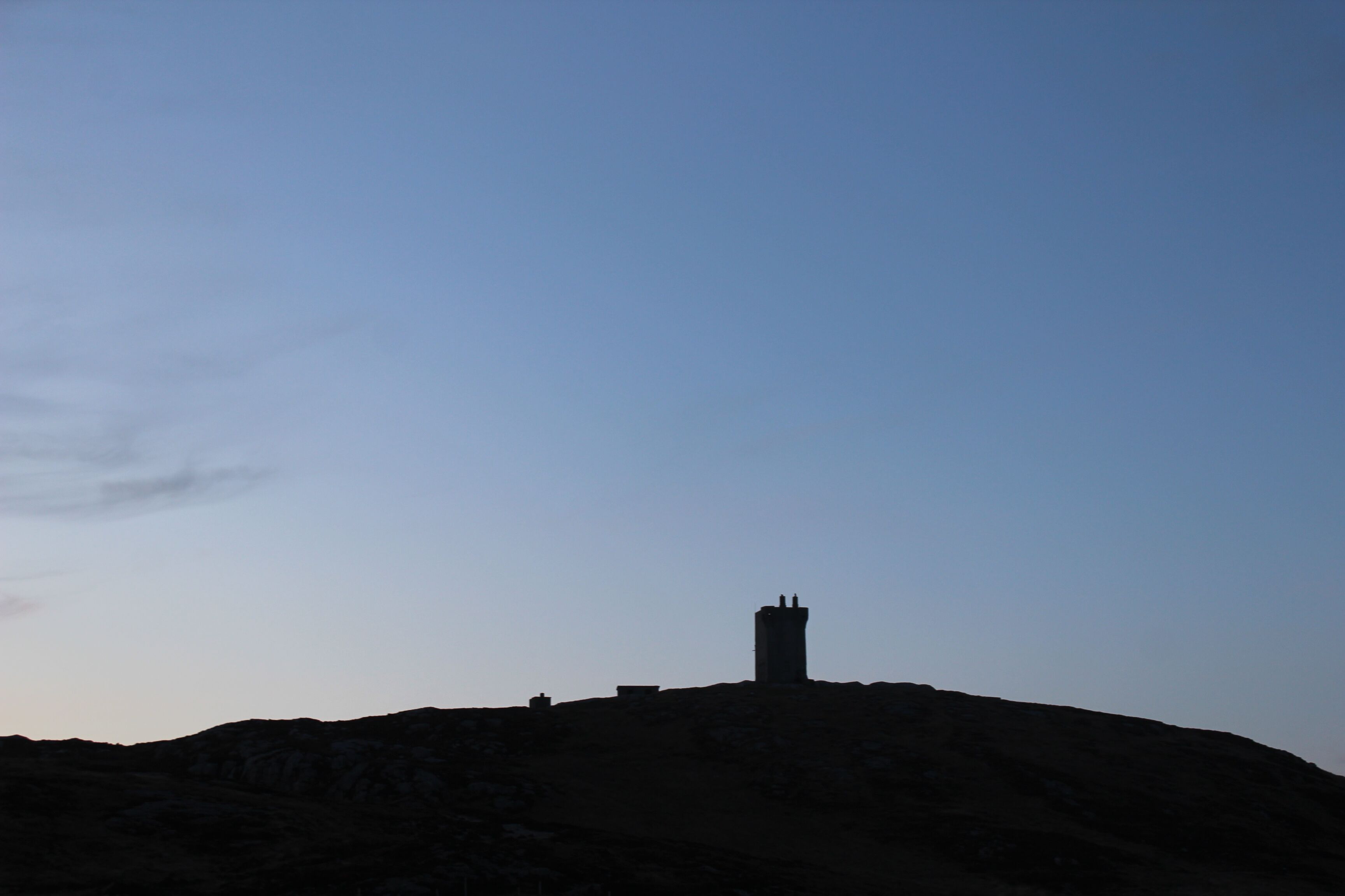Silhouet van een heuvel met een torenachtige constructie erop.