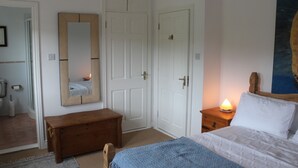 A bedroom with a bed, a wooden bench, a nightstand with a lamp, and a large mirror on the wall. - SolasTobann Room 1 En-suite Malin Head  (Malin Head)