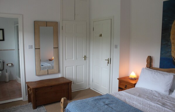 Ein Schlafzimmer mit einem Bett, einer Holzbank, einem Nachttisch mit Lampe und einem großen Spiegel an der Wand.