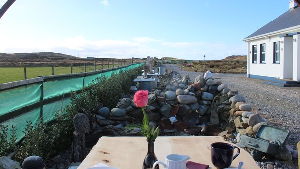 A rustic outdoor dining area with a stone wall, a wooden table, a vase with a single rose, and a clear view of a distant landscape. - SolasTobann Room 1 En-suite Malin Head  (Malin Head)