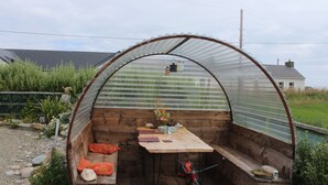 A small, enclosed wooden structure with a table and benches, surrounded by a garden. - SolasTobann Room 1 En-suite Malin Head  (Malin Head)