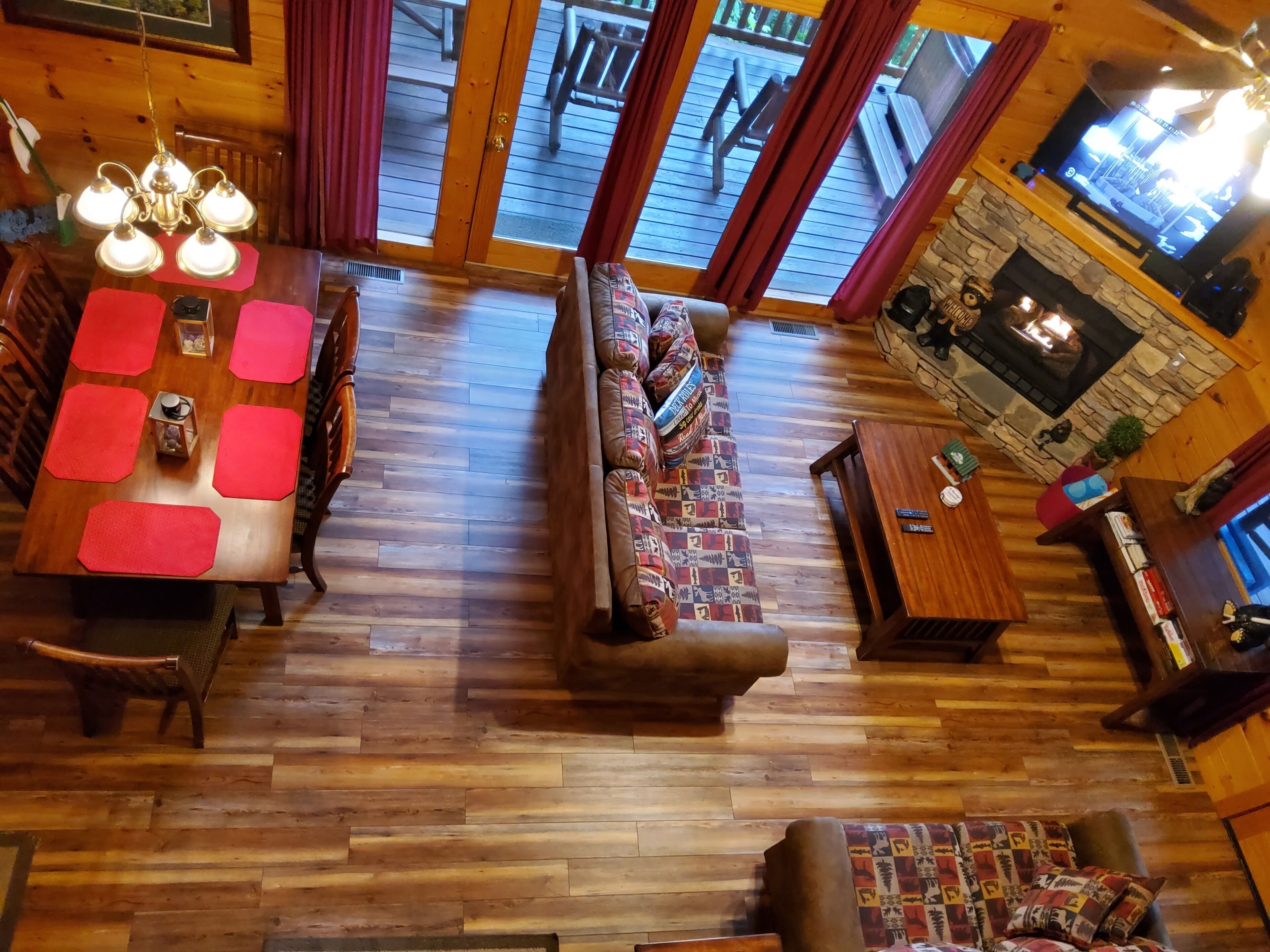 A cozy cabin interior with a wooden dining table, a patterned sofa, a fireplace, and a television.