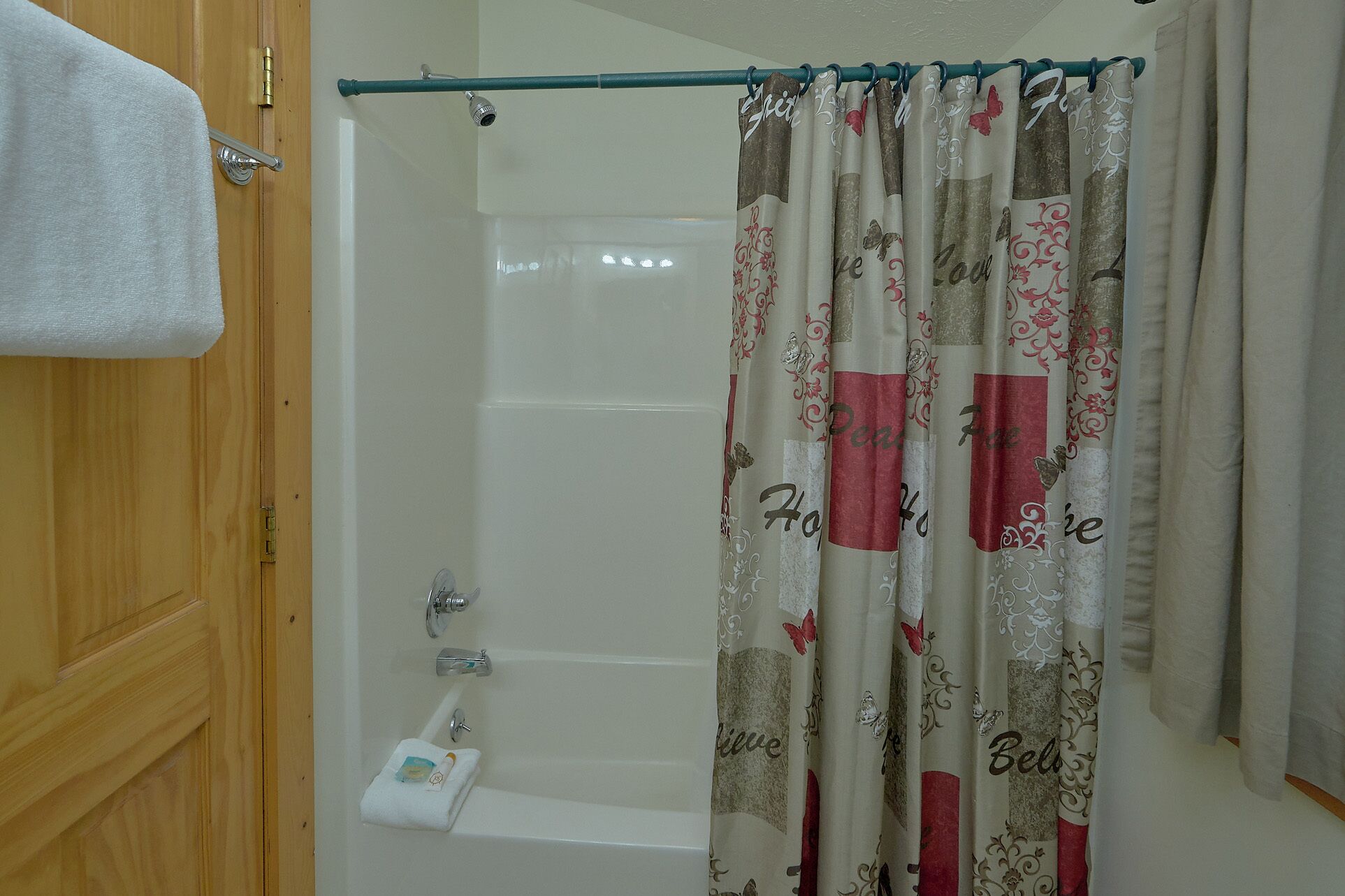 A bathroom with a bathtub, a shower curtain with festive designs, and a towel hanging on the door.