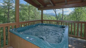 Una vasca idromassaggio su un pontile in legno con vista su una foresta e montagne.