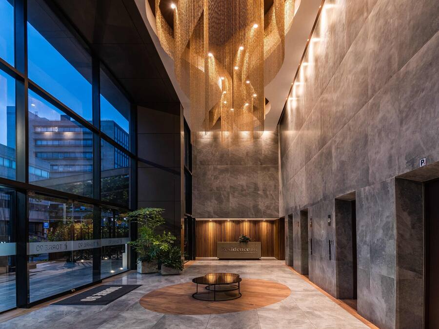 A modern hotel lobby with large windows, a reception desk, and a central seating area.