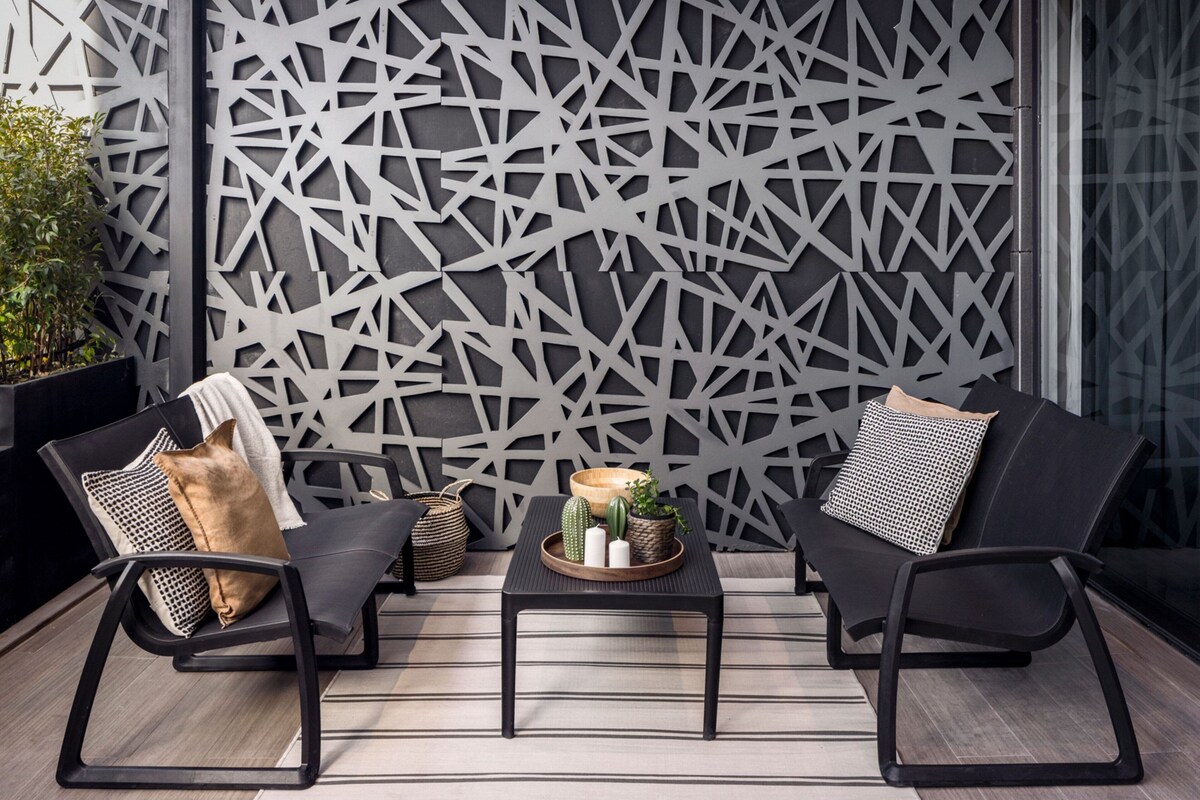A modern outdoor seating area with two black chairs, a small table with decorative items, and a geometric wall design.