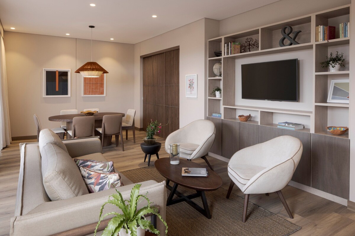 A modern living room with a sofa, armchairs, a coffee table, a TV, and a bookshelf.