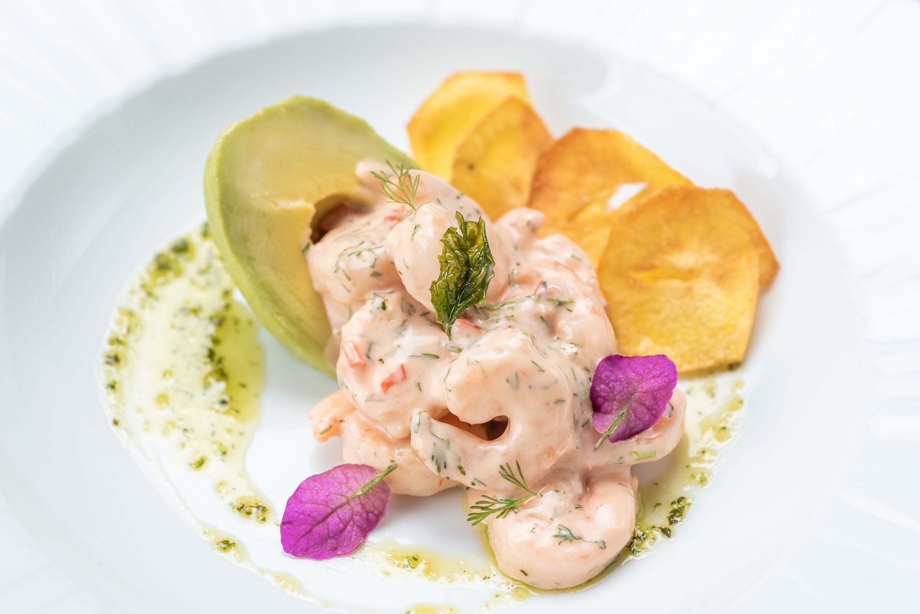 A plate with a creamy seafood dish, avocado, chips, and edible flowers.
