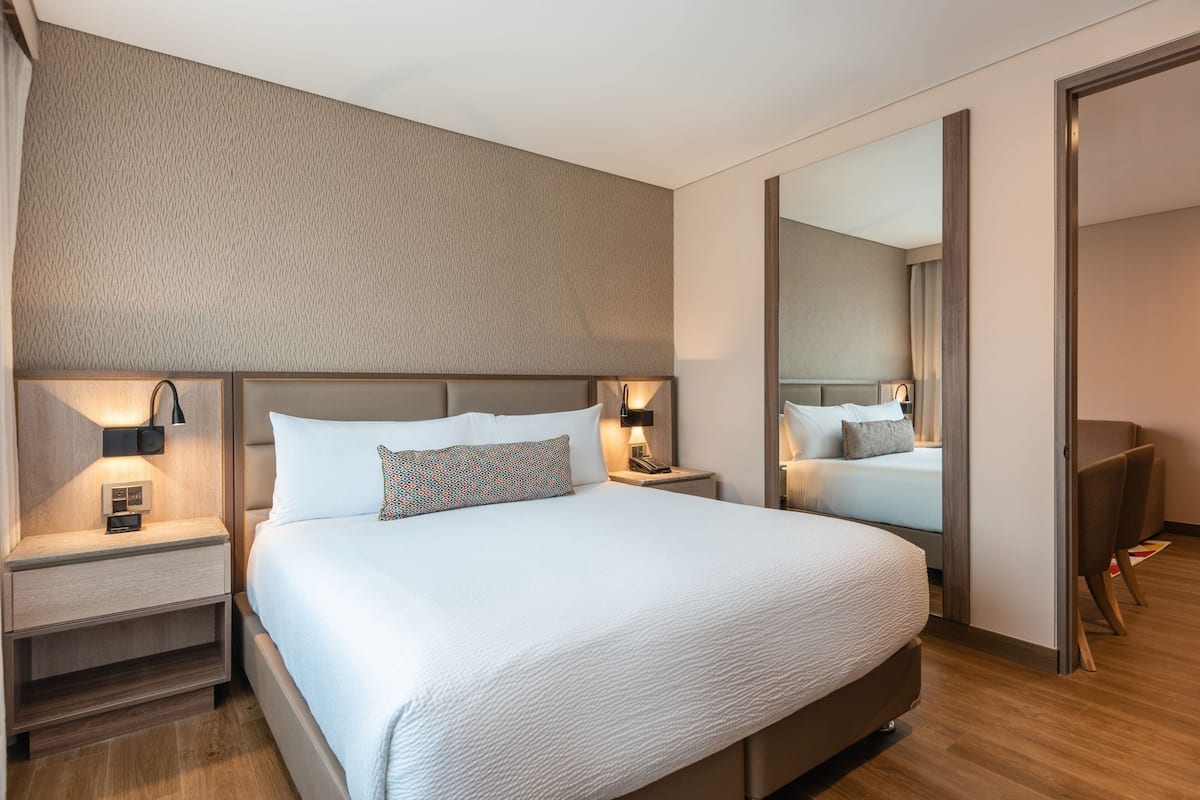 Ett modernt hotellrum med en stor säng, sängbord med lampor, en spegel och en sittgrupp.
