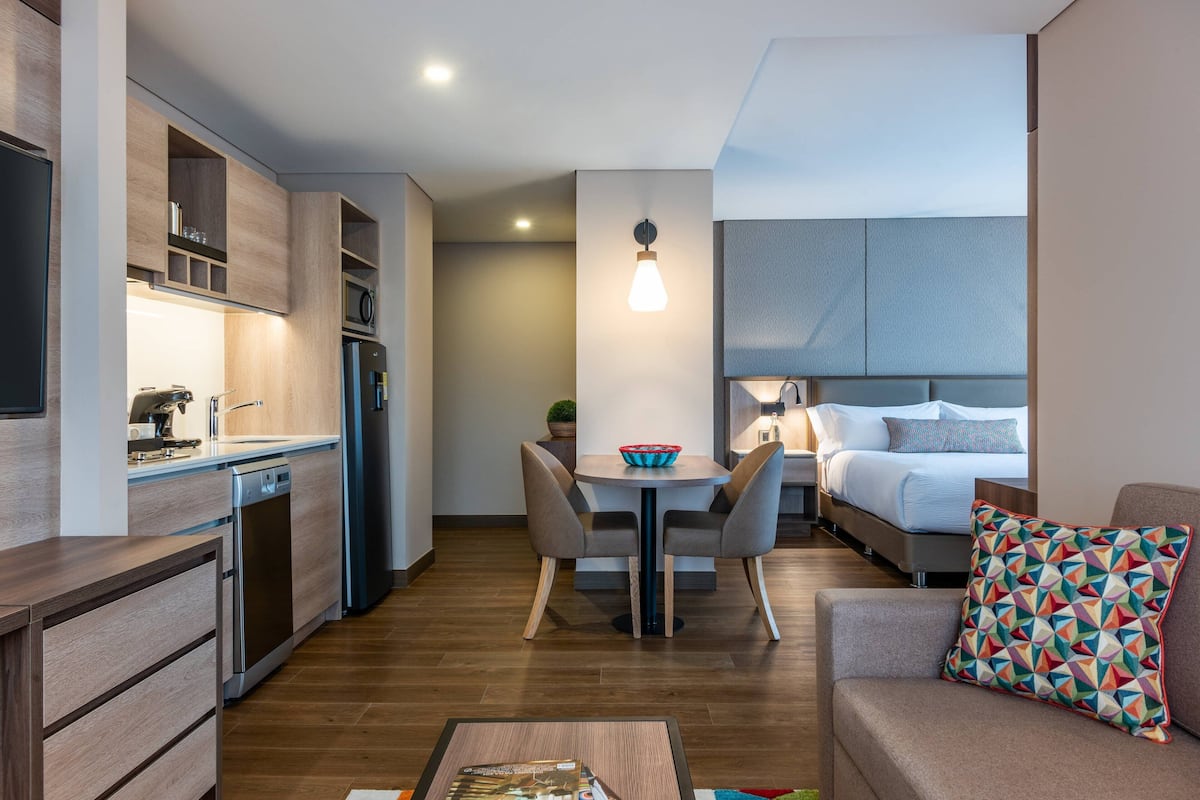 Ett kompakt hotellrum med ett litet kök, en matplats, en säng och en soffa.