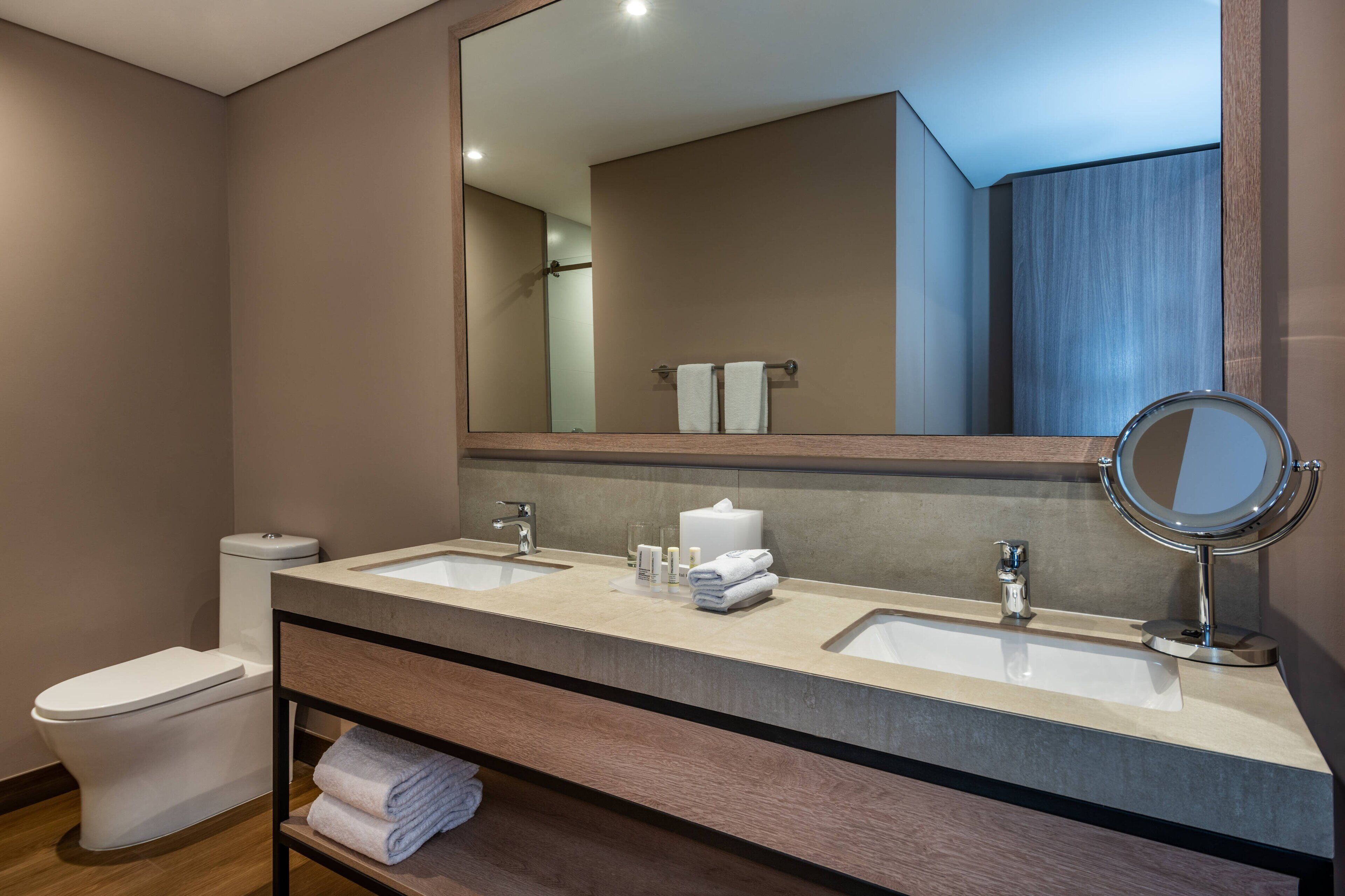Une salle de bain moderne avec deux lavabos, des toilettes, un miroir et un porte-serviettes.