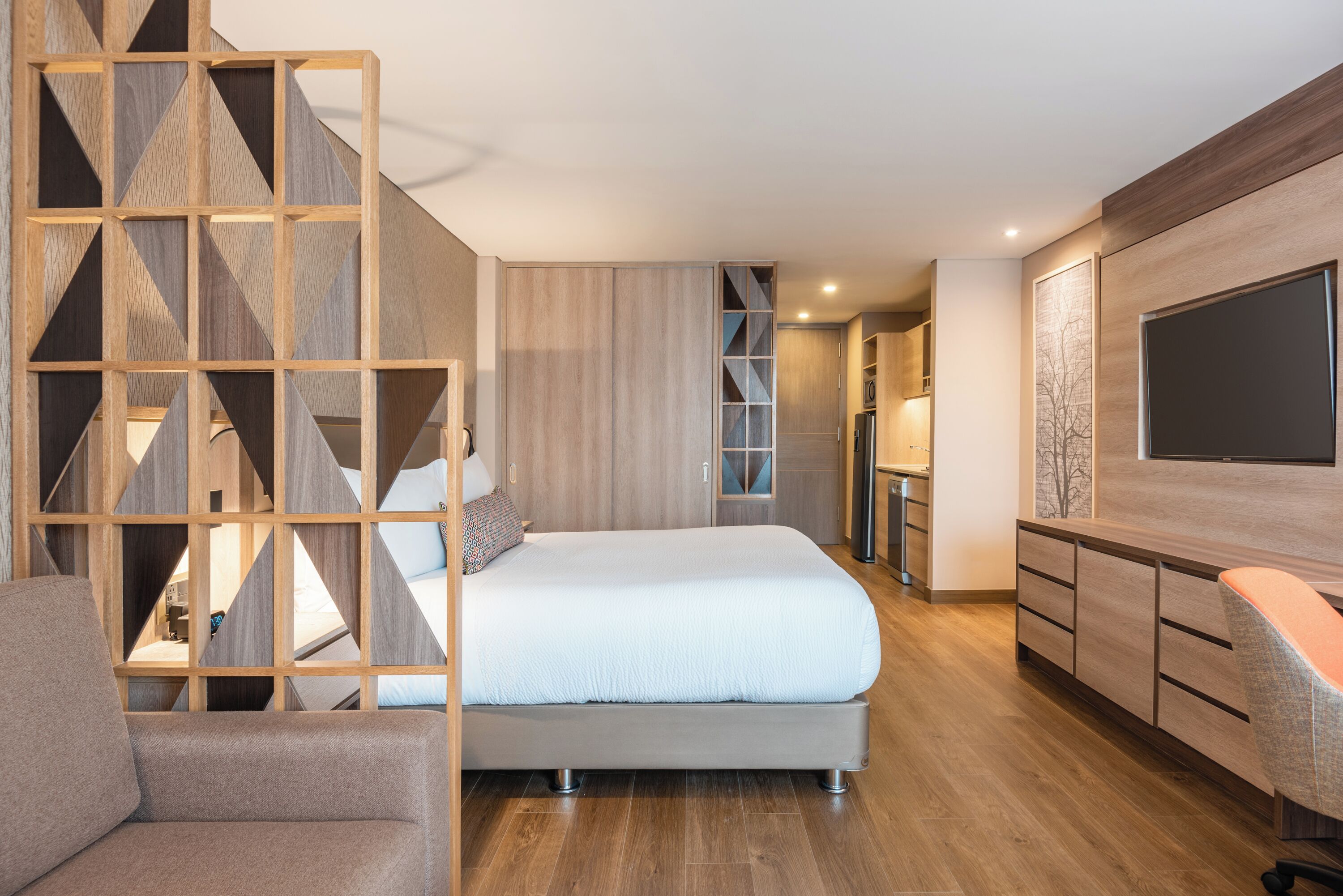 Una habitación de hotel moderna con una cama, un área de descanso, un televisor y un separador de madera.